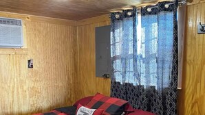 A wooden-paneled room with a bed, a window with patterned curtains, and a small table.