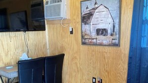 A wooden-paneled room with a dining table, chairs, and a painting of a barn.