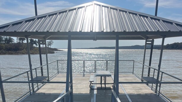 A wooden pier leading to a covered area with a table and benches.