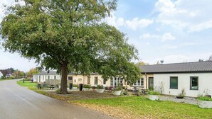 A residential area with a large tree, a paved road, and houses with visible windows and doors. - Holiday Home With Nature View (Gørlev)