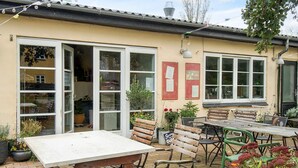 An outdoor patio area with a table and benches, surrounded by potted plants and flowers. - Holiday Home With Nature View (Gørlev)