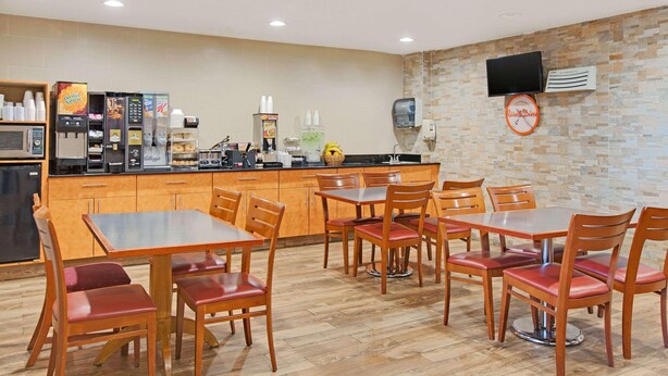 Un restaurante con mesas y sillas de madera, una barra con máquina de café y un televisor montado en la pared.