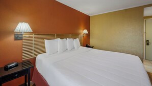 Habitación de hotel con una cama grande, dos lámparas de noche, una mesita de noche con teléfono y una puerta a la derecha.