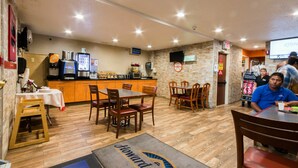 Un restaurante con suelo de madera, mesas, sillas, una barra con una máquina de café y un televisor montado en la pared.