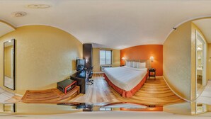 Una habitación de hotel compacta con una cama, un escritorio con computadora, un televisor y un pequeño rincón de descanso.