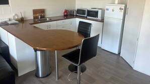 Een kleine keuken met een houten kookeiland, witte kasten, een roestvrijstalen spoelbak, een magnetron, een broodrooster en een koelkast.