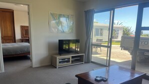 Een woonkamer met een bank, een televisie op een meubelstuk, een eettafel en een grote schuifpui naar een buitenruimte.