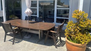 Een terras buiten met een houten tafel en stoelen, een potplant en een witte parasol.
