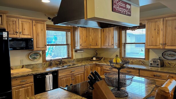 Una cocina con armarios de madera, microondas, lavabo, tostadora y un bloque de cuchillos.
