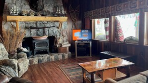 Una sala de estar acogedora con chimenea de piedra, mobiliario de madera y un televisor mostrando un anuncio.
