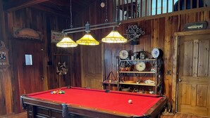 Mesa de billar en una sala de madera con un cartel que indica una edad mínima requerida.