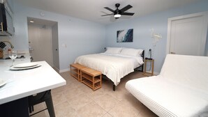 A bedroom with a bed, bedside table, and a small wooden bench. - Casa Playa #104 - Casa Flamingo - Pet Friendly (Fort Myers Beach)