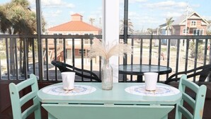 A turquoise table with two chairs on a balcony, with a view of a building and palm trees in the background. - Casa Playa #105 - Sea La Vie - Pet Friendly (Fort Myers Beach)
