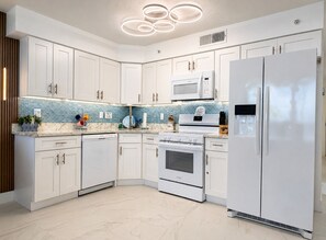 A modern kitchen with white cabinets, a stainless steel refrigerator, a microwave, and an oven.