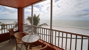 Un balcón con sillas de mimbre y una mesa de vidrio con vista a la playa.