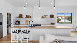 A modern kitchen with a central island, white cabinetry, and a large window offering a view of houses. - The White House - 6 Bennett Street (CARRICKALINGA)