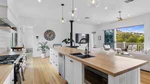 A modern kitchen with a wooden island, white cabinetry, and a large clock on the wall. - The White House - 6 Bennett Street (CARRICKALINGA)