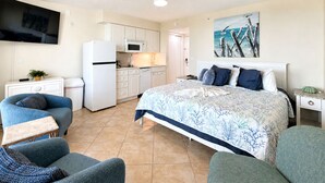 A bedroom with a bed, a TV, a kitchenette, and a ceiling fan. - Casa Playa #404 - Sandy Shores (Fort Myers Beach)