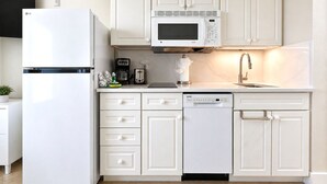 A modern kitchen with white cabinetry, a built-in microwave, a dishwasher, and a refrigerator. - Casa Playa #404 - Sandy Shores (Fort Myers Beach)