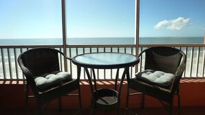Ein Balkon mit Korbstühlen und einem kleinen Tisch, mit Blick auf ein ruhiges Meer.