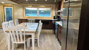 Una cocina moderna con una mesa de comedor, sillas blancas, armarios de madera y un ventanal con vistas a un bosque.