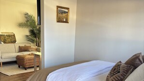 Un dormitorio con una cama de madera, una mesita redonda pequeña y un sofá al fondo.