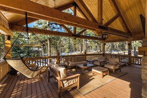 Una terraza de madera con mobiliario exterior, incluyendo sofás y una hamaca, con vistas a una zona boscosa.