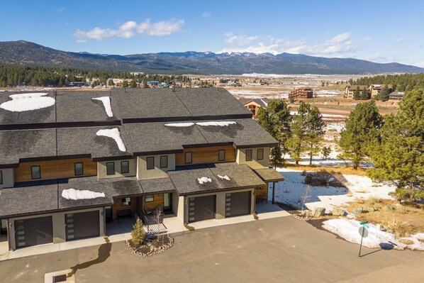A multi-story residential building with a garage, a driveway, and a snow-covered roof. - The Village View Retreat: Steps from the Lift (Angel Fire)