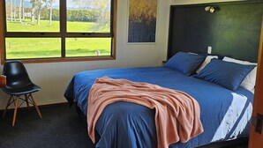 Ein Schlafzimmer mit einem großen Bett, einem Sessel, einem Fenster mit Blick auf Grünflächen und einer Deckenleuchte.