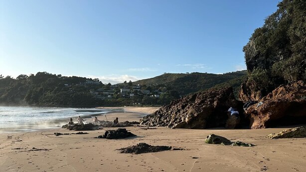 Ein sandiger Strand mit Fußabdrücken, eine felsige Klippe und ein klarer, blauer Himmel.