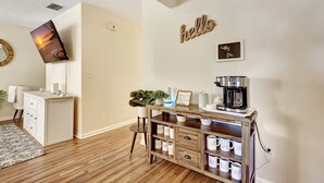 A cozy living room with a coffee station, a TV mounted on the wall, and a 'hello' sign. - Coastal Comfort 4BR in Stuart FL (Stuart)