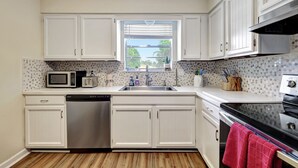 A compact kitchen with white cabinets, a dishwasher, a microwave, a toaster, a sink, and a stove. - Coastal Comfort 4BR in Stuart FL (Stuart)