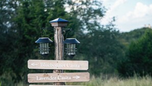 A wooden directional signpost with lanterns, surrounded by a garden with orange flowers and a stone cross at the base.