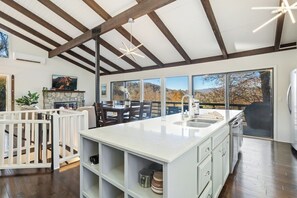 A spacious kitchen with a large island, wooden beams, and a view of the outdoors. - Pet-Friendly Mountain Cabin with Hot Tub Near Sugar Mountain, Sleeps 12 (Sugar Mountain)