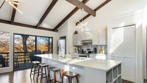 Una cocina moderna con una isla grande, taburetes de bar y vistas a árboles a través de amplios ventanales.