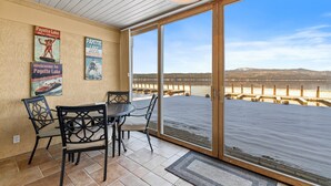 Un patio cubierto con mesa y sillas, vista a un lago y carteles en la pared.