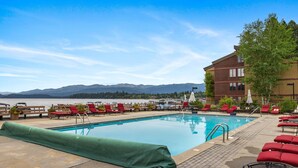 Zona de piscina con sillas de descanso rojas, piscina techada y vistas a montañas y un lago.