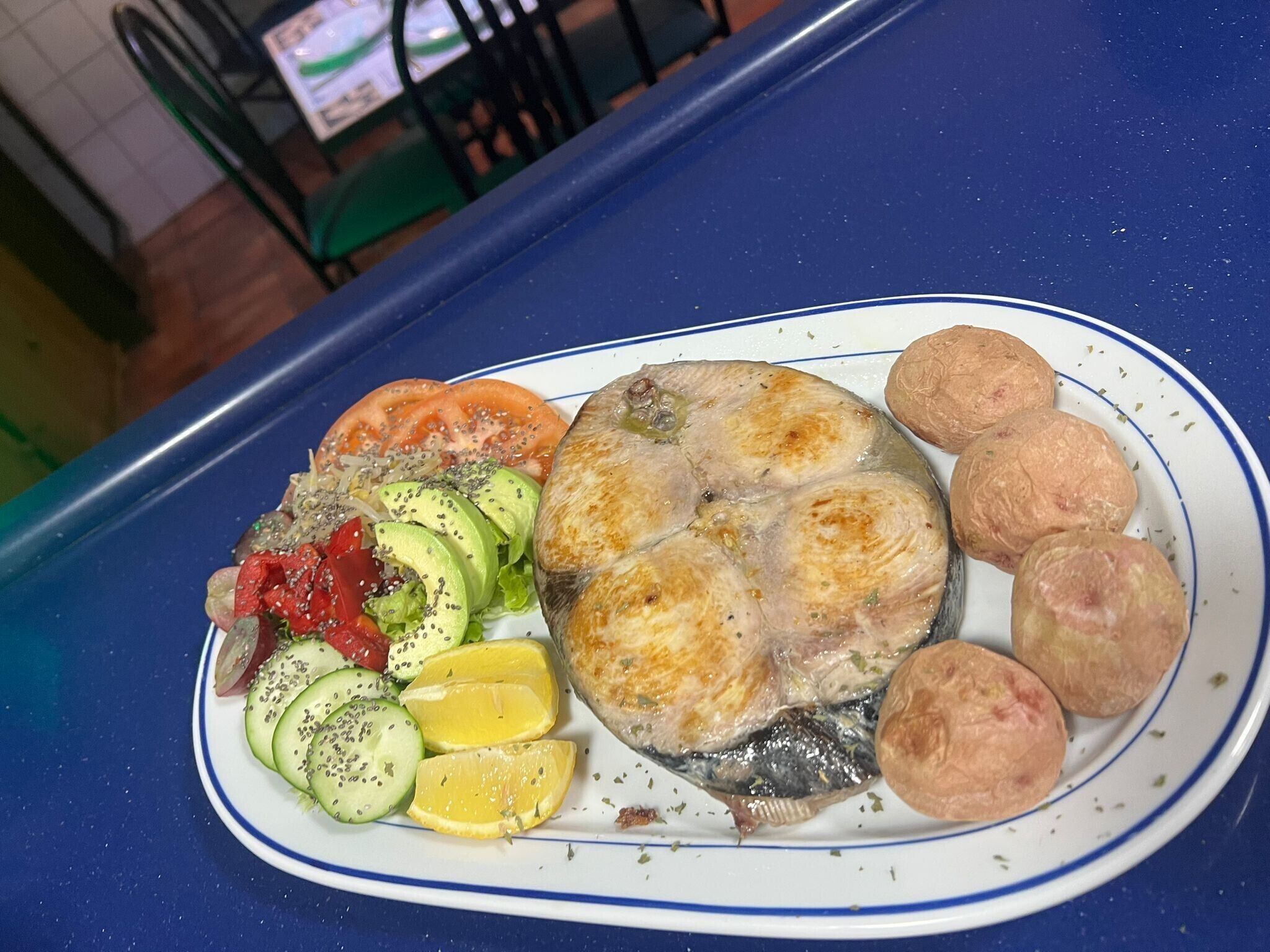 A plate with fish, vegetables, and bread on a blue table.