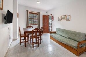 A room with a dining table and chairs, a sofa, a television, and a fire extinguisher.