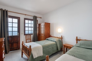 A bedroom with two wooden beds, a wooden wardrobe, a chair, and a bedside table.