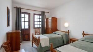 Ein Schlafzimmer mit zwei Betten, einem Holzschrank, einem Stuhl und einem Fenster mit Vorhängen.