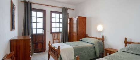 A bedroom with two beds, a wooden wardrobe, a chair, and a window with curtains.
