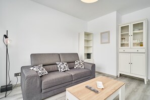 Ein modernes Wohnzimmer mit grauem Sofa, einem Holztisch, einem weißen Schrank und einer Stehlampe.