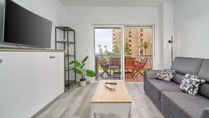 Una sala de estar moderna con un televisor de pantalla plana, un sofá, una mesa de centro y un balcón con mobiliario exterior.