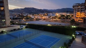 Cancha de tenis con edificios aledaños y una montaña al fondo.