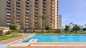 Una piscina con solárium de baldosas, rodeada por un edificio residencial alto con balcones.