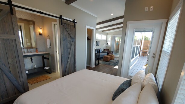 A bedroom with a large bed, a bathroom with a sink and mirror, and a view of a deck and outdoor area.