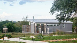 A modern, single-story building with a metal roof, surrounded by a landscaped garden with a paved walkway.