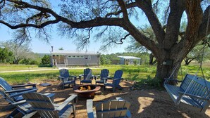 A patio area with Adirondack chairs, a fire pit, and a large tree.
