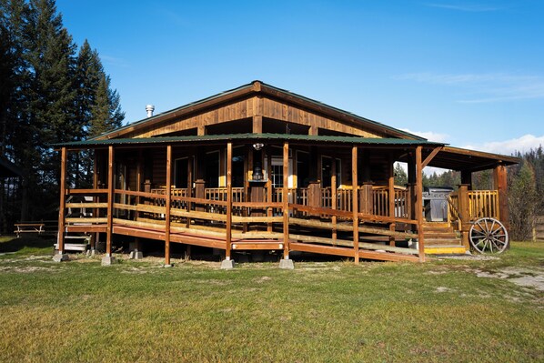 Eine Holzhütte mit Veranda, überdachter Außenbereich und einem großen Wagenrad.